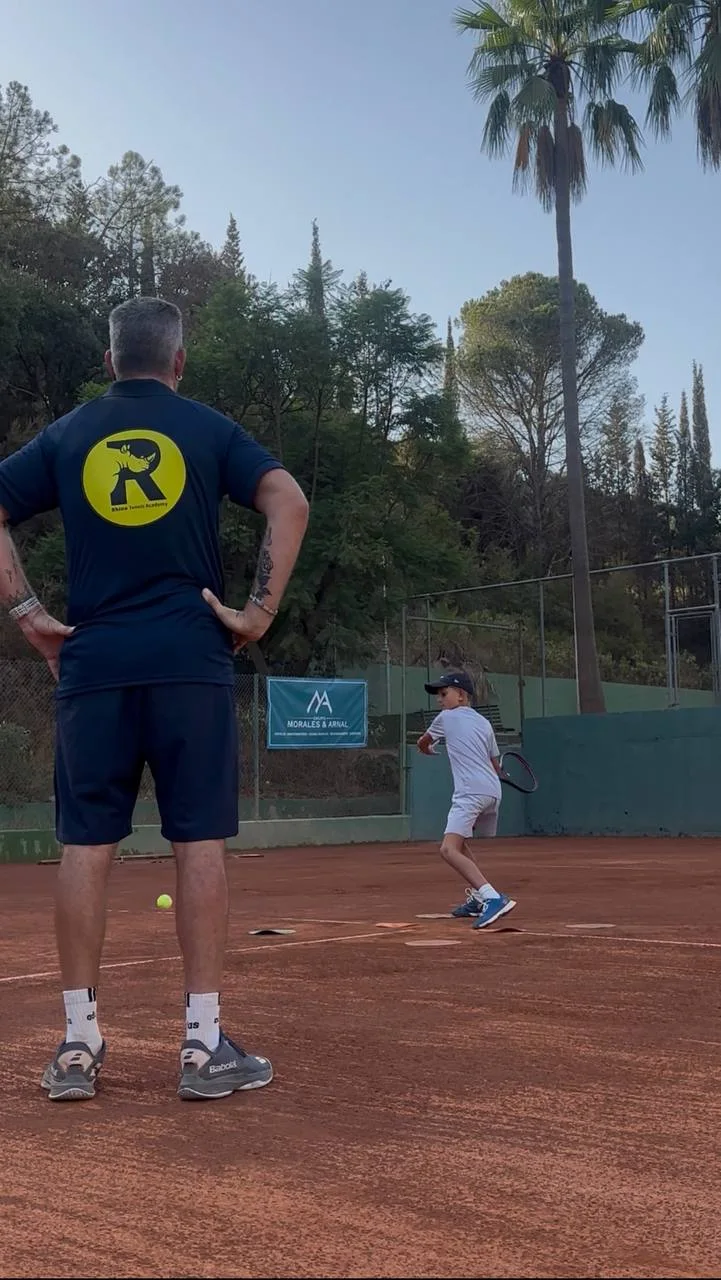 Rhino coach watching a young player practise on a clay court